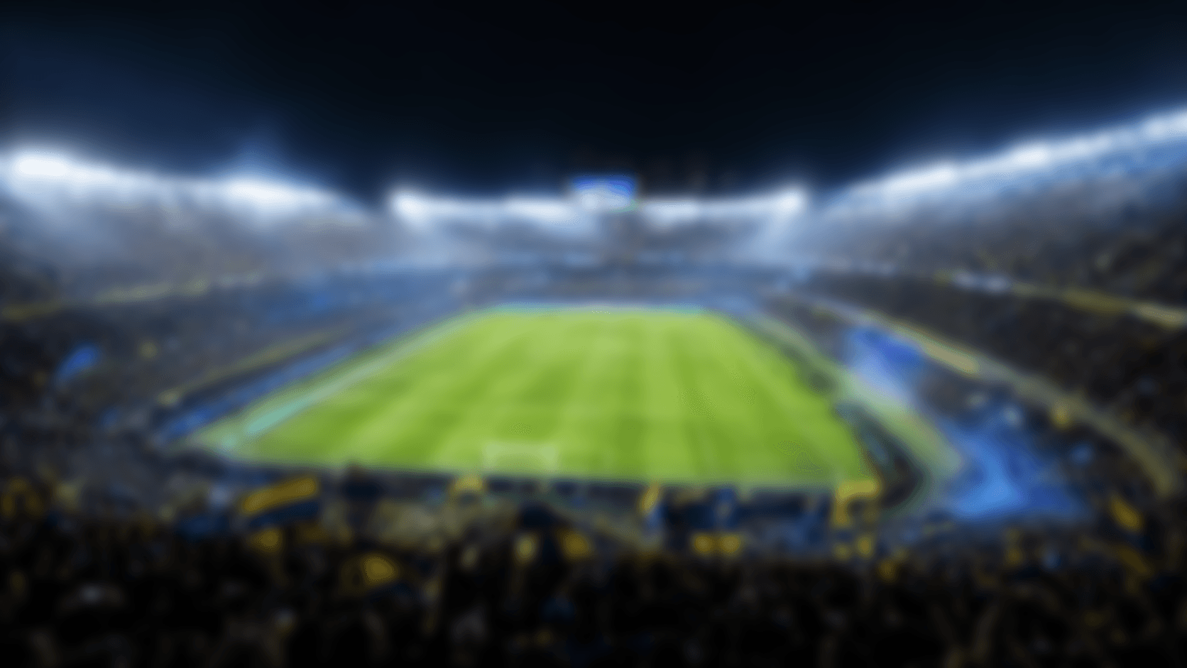 Blurred soccer stadium at night with green pitch and crowd under floodlights