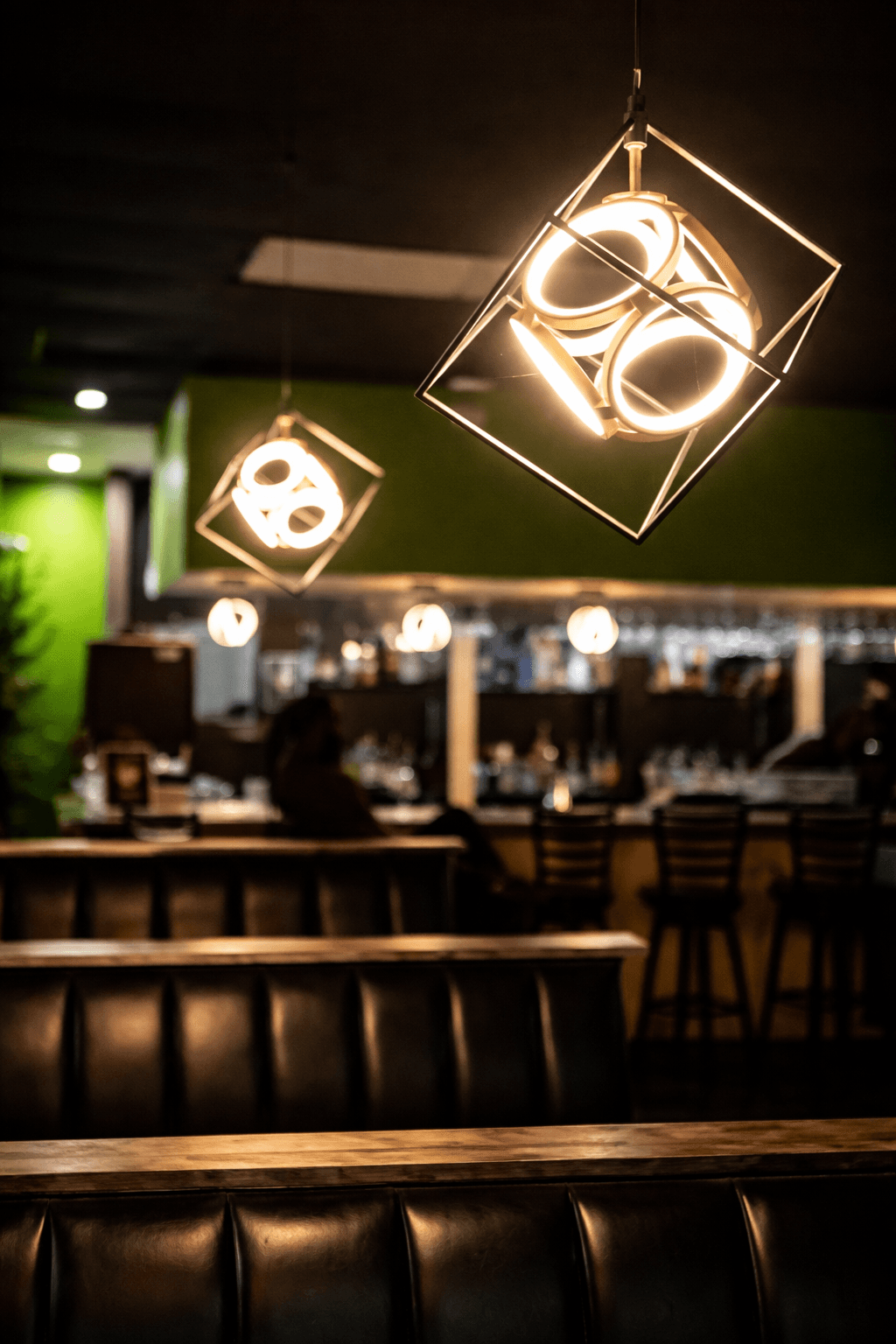 MOV lounge at night—geometric pendant lights, bar glow, and deep booth seating